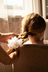 Close-up of mother hands weaving a delicate braid in her daughter's fine hair. Tender moment of feminine connection and care.