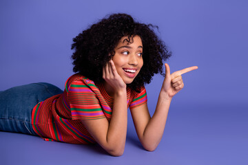 Young smiling woman lying on violet background, wearing colorful casual attire, making a friendly...