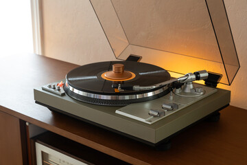 Vintage Stereo Turntable Record Player With Black Disk and Weight Clamp Sitting on Wooden Console...