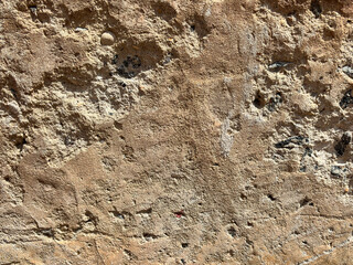 Textured surface of weathered stone wall in sunlight revealing natural patterns and subtle colors