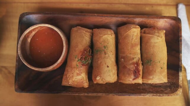 Crispy spring rolls served on wooden tray with savory dipping sauce on cafe table