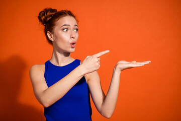 Young woman with red hair gesturing towards empty space against an orange background