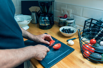Close Up of Senior Mans Hands Preparing Fresh Tomato in Bright Modern Kitchen
