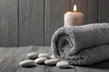 Rolled gray towel, stones, candle on gray wood