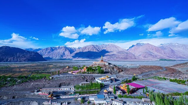 Timelapse A breathtaking wide-angle view of Diskit Monastery crowned by the towering Maitreya Buddha statue, nestled in the dramatic Nubra Valley with the Himalayas forming a majestic backdrop