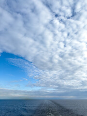 White cotton clouds and a sea trail left by a ferry.