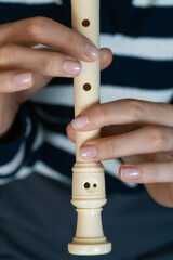 Close-up of hands playing a recorder flute, practicing music in a home environment, with a blurred background suggesting a comfortable and focused learning experience. Vertical photo © Volha