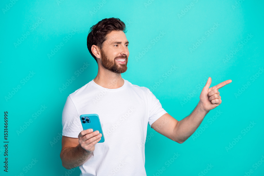 Poster casually dressed man holding a phone and pointing on a teal background in a modern and stylish gestu