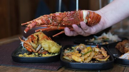 Grilled lobster on a tray with vegetables, vibrant plating, seafood dining experience. holding half a lobster in hand