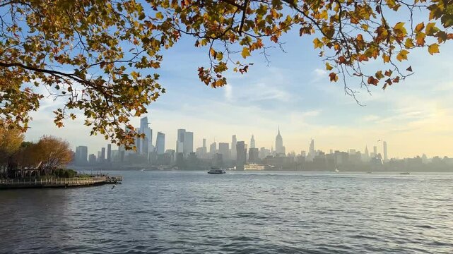 Peaceful video of the Manhattan skyline seen from Hoboken on a crisp autumn morning. Fall leaves frame the cityscape as a boat passes under soft golden light.

