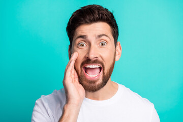 Excited young man shouting with a hand gesture on a turquoise background wearing a white t-shirt and smiling