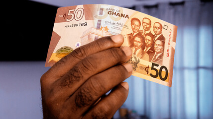 Close up of Black person hands raising showing pointing, inspecting and checking 50 Ghanaian cedi note. watermark.inspection of money. Verification of paper currency not fake counterfeit original real