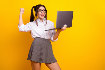 Happy student in white shirt with laptop celebrating success against bright yellow background