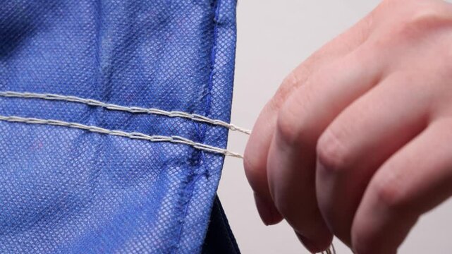 Close-up slow motion of a seamstress using a seam ripper to remove stitches from a piece of blue fabric
