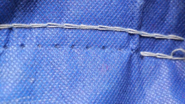 Precise handheld seam ripper carefully detaching white stitches from vibrant blue fabric, capturing delicate process of garment alteration in crisp slow motion