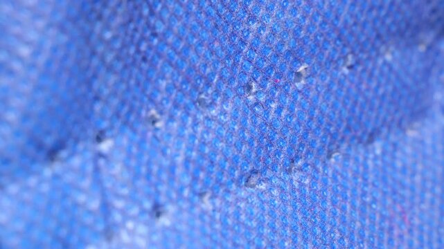 White thread pulling through blue fabric in slow motion