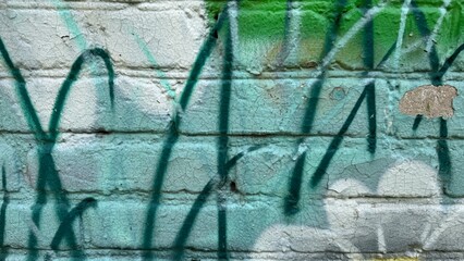Graffiti on a mint green brick wall, featuring dark spray paint lines and faint white shapes