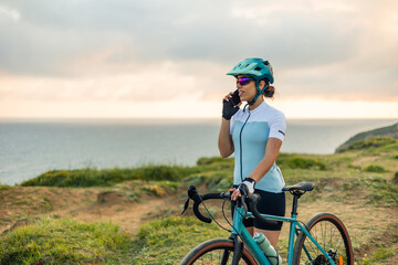 Latin cyclist woman using smartphone on gravel bike near the sea at sunrise