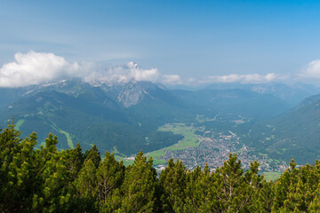 Hiking above the clouds on Wankberg, Germany—panoramic views of snow-capped Alps and lush valleys under a bright blue sky.