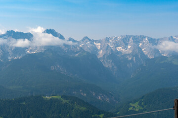 Hiking above the clouds on Wankberg, Germany—panoramic views of snow-capped Alps and lush valleys under a bright blue sky.