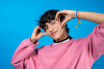 Young latin man wearing lgbt bracelet making a funny face with hands near head