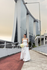 Smiling bride in elegant dress holding bouquet with Marina Bay Sands in background Singapore