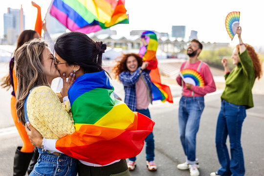 Lesbian couple kissing on LGBTQ parade festival. Two young girlfriends in love. Diverse people of gay and lesbian community celebrating lgbt pride day