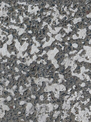 A close-up view of a weathered asphalt surface with scattered patches of peeling white paint and rough, textured stones.