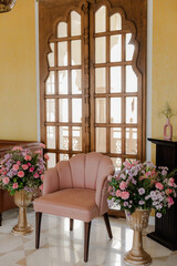 Elegant pink armchair with floral arrangements in a classically designed room.