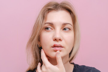 Fototapeta premium Young woman with virus herpes touching lips against pink background. Herpes blisters