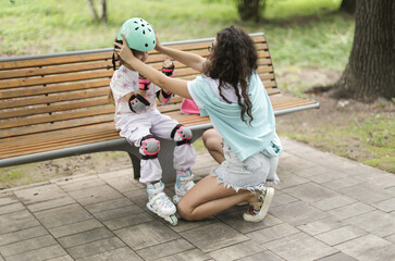 mother putting a helmet on her daughter before rollerblading. Safety first! A loving and caring moment on a bench in a green park.