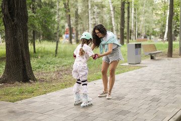 Mother teaching her daughter how to rollerblade in a park. The girl wears protective gear and helmet. A joyful and bonding outdoor moment filled with love and support.