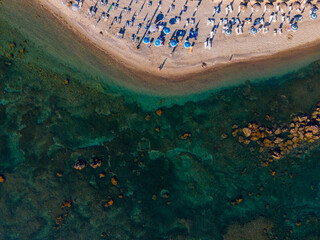High-angle drone photograph of a beautiful sandy beach lined with white sunbeds and blue umbrellas....