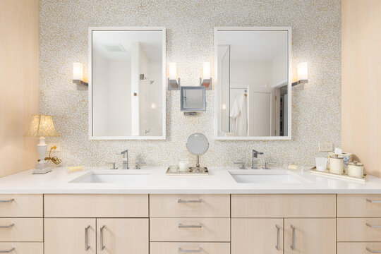 A bathroom detail with wood cabinets, pattern tile backsplash, chrome faucets, and decorations on a white marble countertop. No brands or labels.
