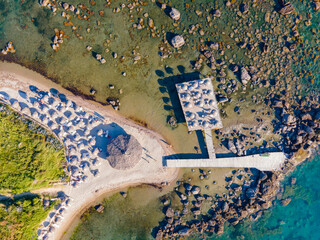 High-angle drone photograph of a beautiful sandy beach lined with white sunbeds and blue umbrellas....