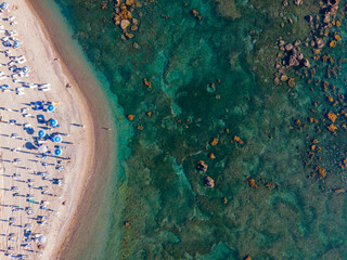 High-angle drone photograph of a beautiful sandy beach lined with white sunbeds and blue umbrellas....