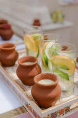 Refreshments: Small terracotta pots with white liquid and glass beverages with fruit slices on a decorative tray create a refreshing and inviting scene.
