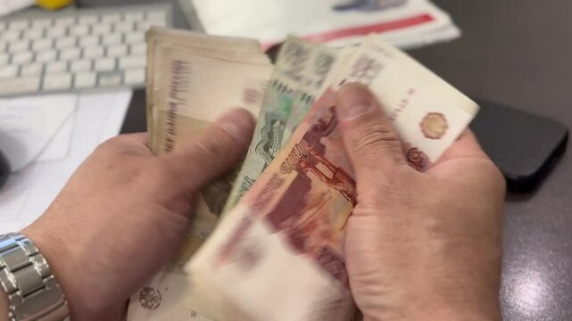 A man holds a wad of money in his hands. A close-up of a man's hands counts a bundle of bills for five thousand Russian rubles. Man counts red paper 5000 rubles bills. Russian cash money in male hand.