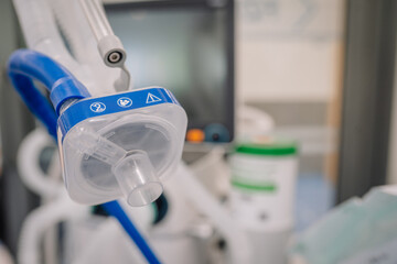 Close-up of a transparent medical breathing mask with blue tubing connected to a ventilator system...