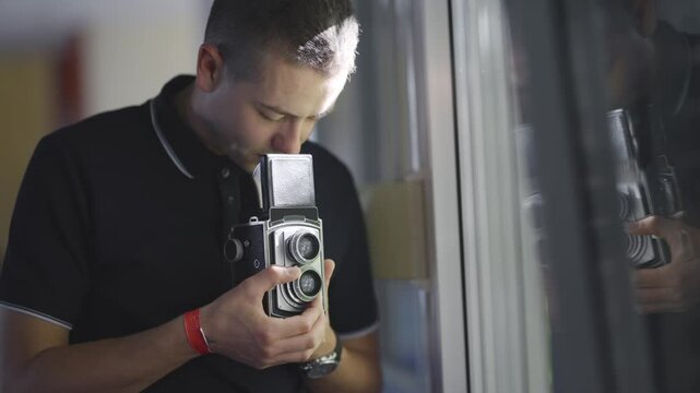 Photographer man capturing images using a vintage retro twin-lens reflex camera by a window
