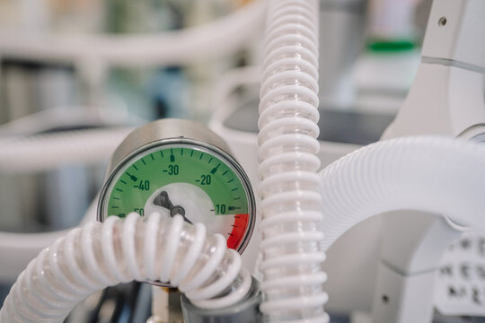 Close-up of a vacuum pressure gauge with coiled medical hoses in a hospital setting, displaying negative pressure values in green and red zones.