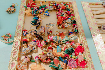 A collection of handmade doll keychains with intricate, colorful clothing displayed on a decorative tray, showcasing craftsmanship and vibrant folk art.