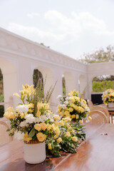 Elegant yellow & white floral arrangements on a wooden table, creating a refined outdoor setting perfect for events or celebrations.