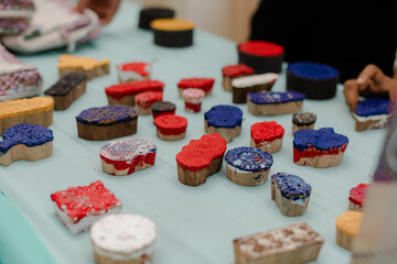Assortment of wood block prints. Wood stamps with red, white, blue, yellow, and black ink are displayed on a light table surface.