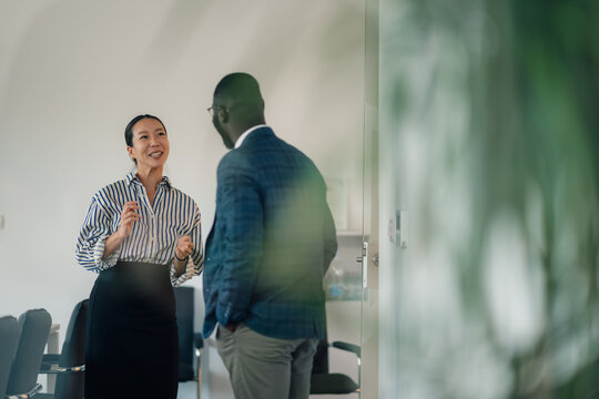 Businesswoman gesturing while talking to businessman in office hallway