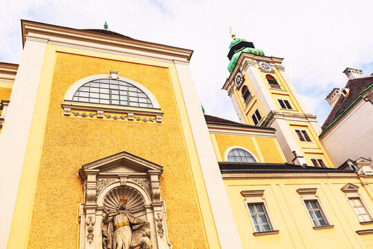 Schottenkirche in Vienna stands with a bright yellow Baroque facade, framed by arched windows and a central statue niche. Its clock tower, topped with a green roof, rises above the historic cityscape