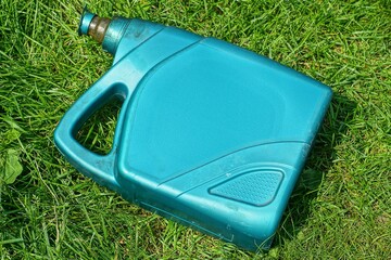 one plastic green dirty with lid closed industrial with handle empty modern discarded canister lies in the grass during the day on the street