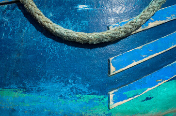 Close-up of a blue wooden fishing boat in Essaouira, Morocco. Weathered paint, wood texture, and a rope create a nautical abstract with vibrant blue and green tones