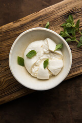 Whole tied Italian cheese burrata on small wooden cutting board served with fresh oregano