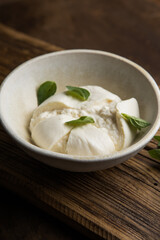Whole tied Italian cheese burrata on small wooden cutting board served with fresh oregano